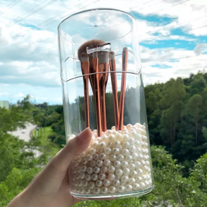 Transparent container filled with white beads and brown makeup brushes
