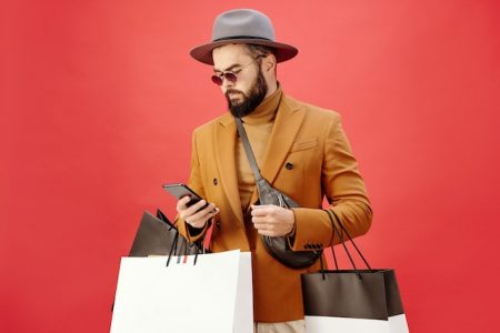 Young adult looking at his phone and carrying multiple shopping bags