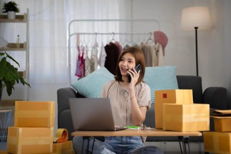smiling-happy-young-asian-woman-entrepreneur-receiving-phone-call-new-sales-order-among-boxes-product-with-laptop-computer
